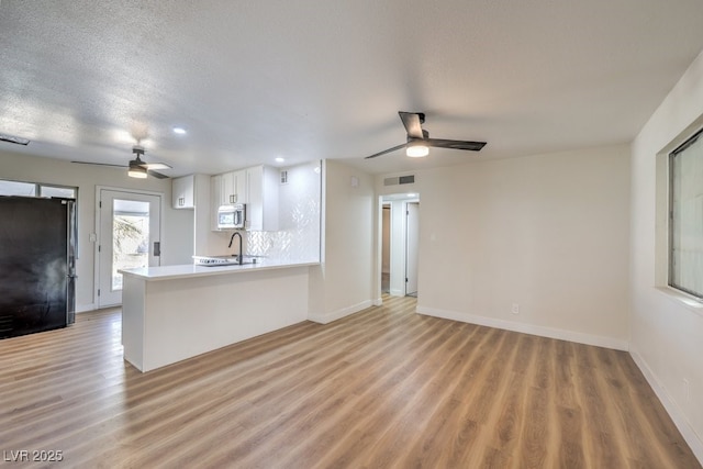 interior space with kitchen peninsula, black fridge, light hardwood / wood-style flooring, and white cabinetry