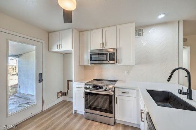 kitchen with white cabinets, appliances with stainless steel finishes, decorative backsplash, sink, and light wood-type flooring