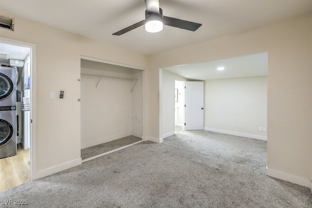 unfurnished bedroom featuring ceiling fan, light colored carpet, stacked washer / dryer, and a closet