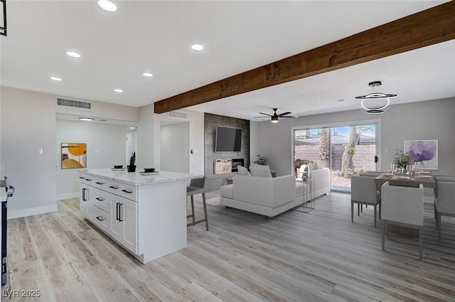 kitchen featuring light stone countertops, white cabinets, a kitchen island, light wood-type flooring, and beam ceiling