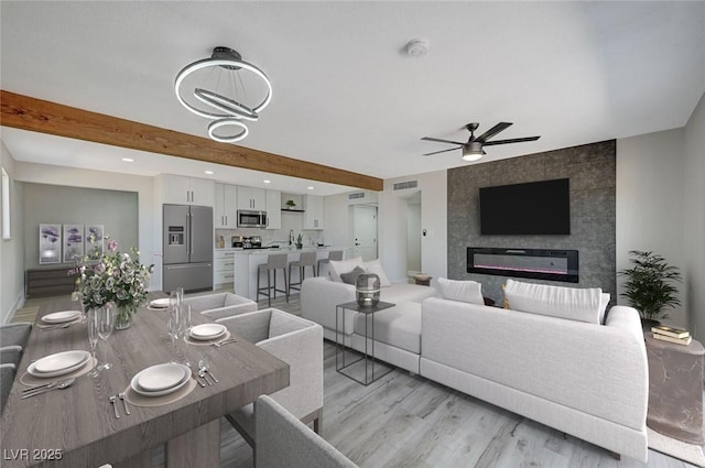 living room featuring beamed ceiling, a large fireplace, sink, light hardwood / wood-style flooring, and ceiling fan