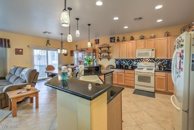 kitchen with white appliances, decorative light fixtures, light brown cabinets, sink, and a center island with sink