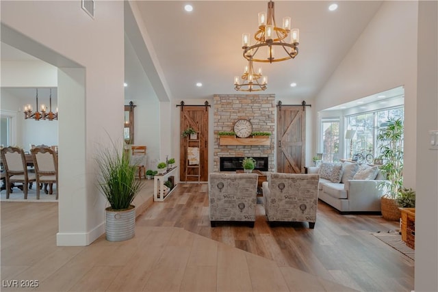 living room with light wood-type flooring, a chandelier, a barn door, and high vaulted ceiling