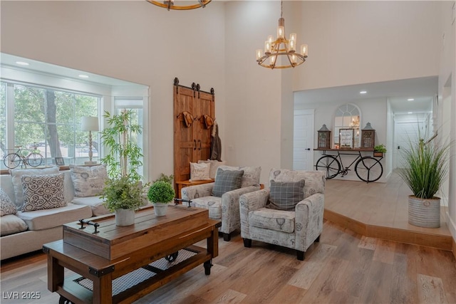 living room with an inviting chandelier, light hardwood / wood-style flooring, a towering ceiling, and a barn door