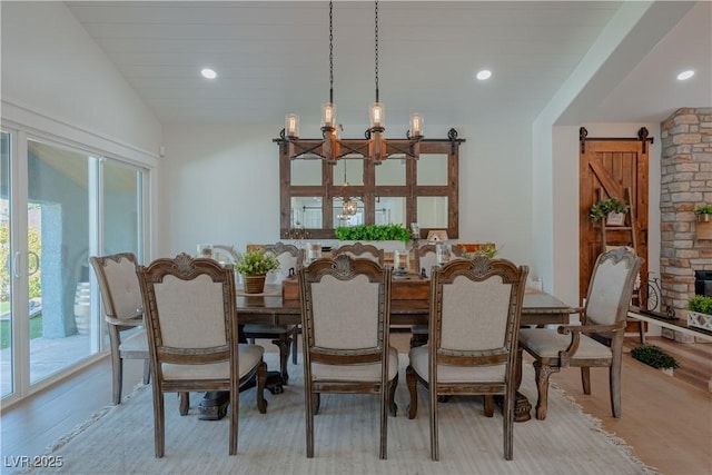 dining room with vaulted ceiling, a barn door, and light hardwood / wood-style flooring