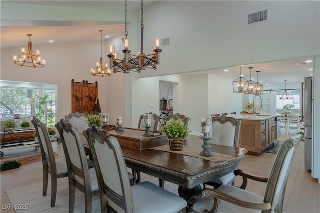 dining space featuring light hardwood / wood-style flooring, sink, a barn door, high vaulted ceiling, and a chandelier