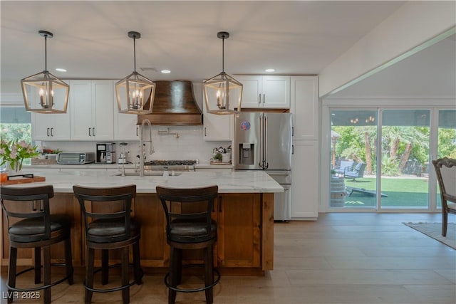 kitchen with light stone countertops, white cabinets, stainless steel fridge with ice dispenser, and custom range hood