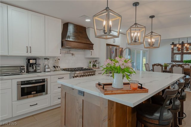 kitchen featuring decorative light fixtures, white cabinetry, a center island with sink, and custom exhaust hood