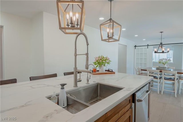 kitchen featuring sink, hanging light fixtures, a barn door, and light stone counters