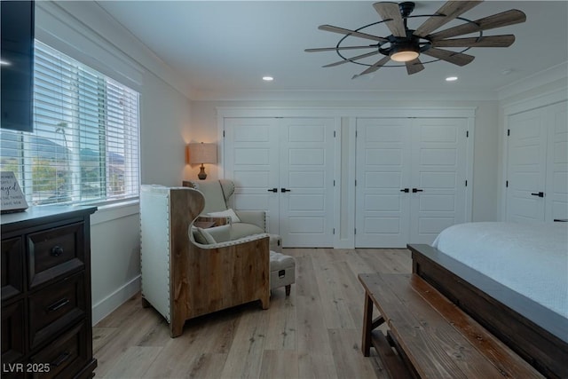 bedroom with light hardwood / wood-style floors, two closets, ceiling fan, and ornamental molding