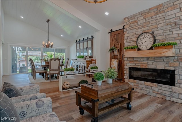 living room featuring a fireplace, a chandelier, light wood-type flooring, high vaulted ceiling, and a barn door