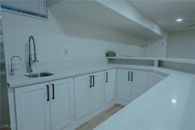 interior space with sink, white cabinetry, light hardwood / wood-style flooring, and light stone countertops