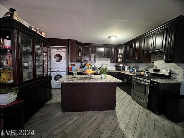 kitchen featuring stacked washer / dryer, a center island, light stone counters, dark brown cabinets, and stainless steel range with gas stovetop