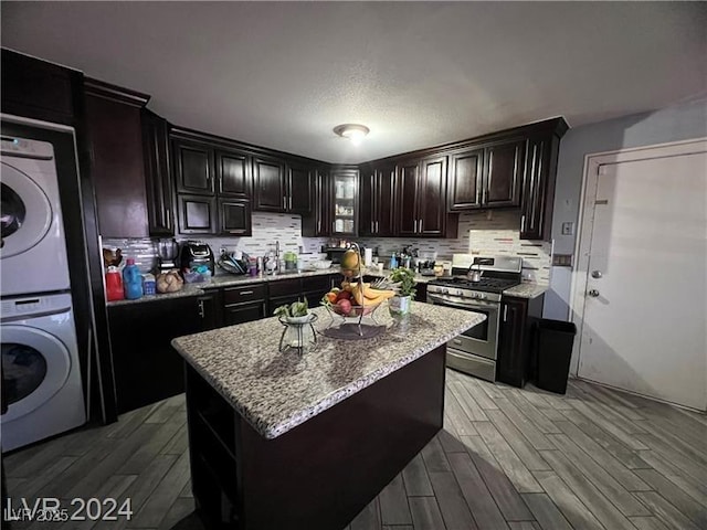 kitchen featuring dark brown cabinetry, gas stove, a center island, stacked washing maching and dryer, and light stone countertops