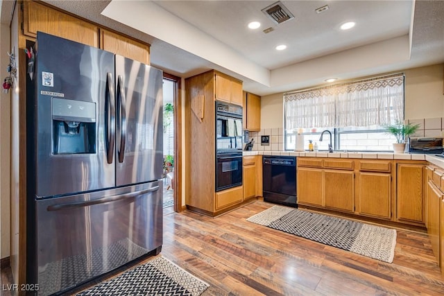 kitchen featuring black appliances, a raised ceiling, light hardwood / wood-style flooring, backsplash, and tile countertops