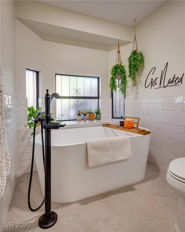 bathroom featuring a washtub, tile walls, toilet, and tile patterned flooring