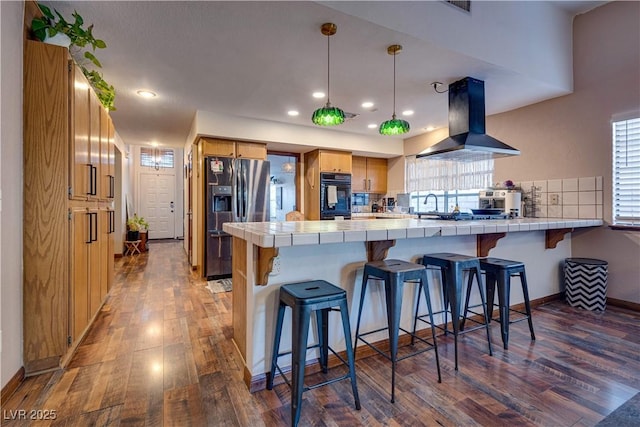 kitchen featuring tile counters, black oven, a kitchen breakfast bar, kitchen peninsula, and island range hood