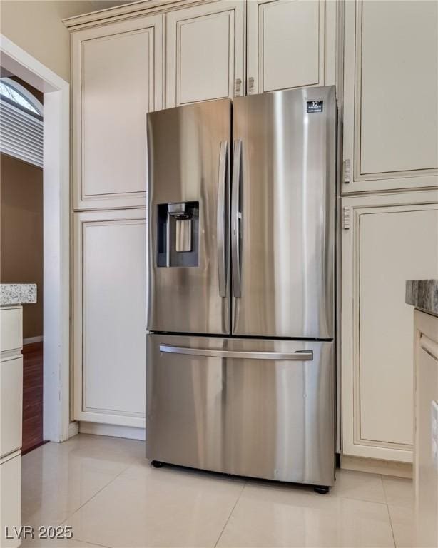 kitchen with stainless steel fridge with ice dispenser, cream cabinets, light stone countertops, and light tile patterned floors