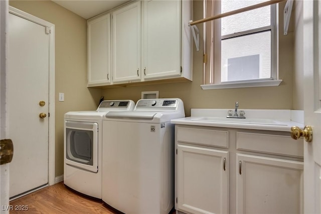 washroom featuring cabinets, sink, washing machine and dryer, and light wood-type flooring