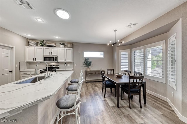 dining area with sink, light wood-type flooring, and an inviting chandelier