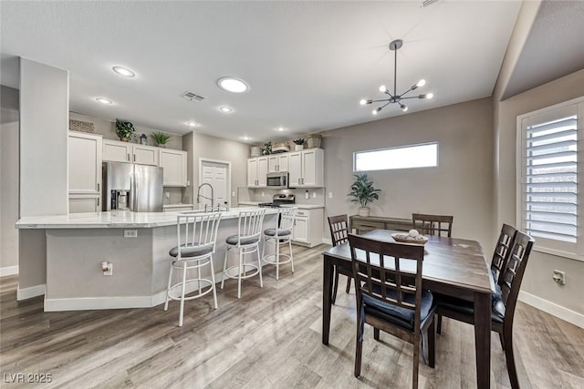 dining space with light hardwood / wood-style floors, sink, and a chandelier