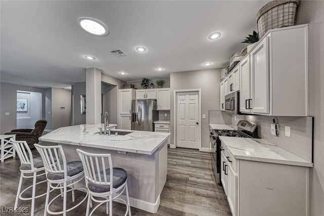 kitchen featuring appliances with stainless steel finishes, sink, white cabinets, an island with sink, and light stone counters