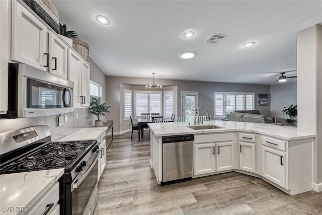 kitchen featuring kitchen peninsula, appliances with stainless steel finishes, sink, white cabinets, and tasteful backsplash