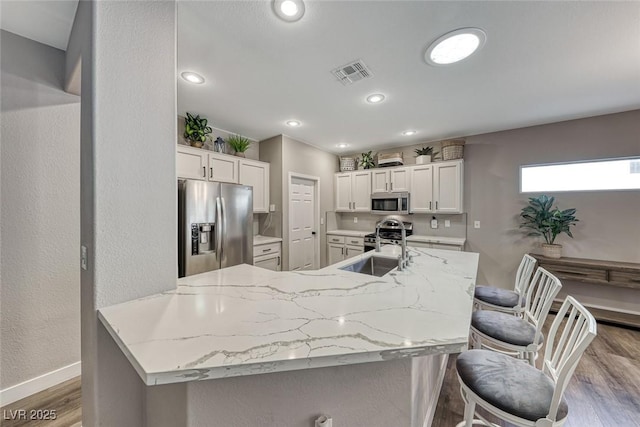 kitchen with white cabinets, sink, a breakfast bar, stainless steel appliances, and light stone counters