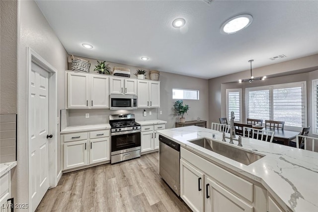 kitchen with sink, white cabinets, light wood-type flooring, light stone counters, and stainless steel appliances