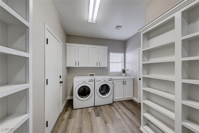 laundry room with light hardwood / wood-style floors, cabinets, a textured ceiling, and washing machine and dryer