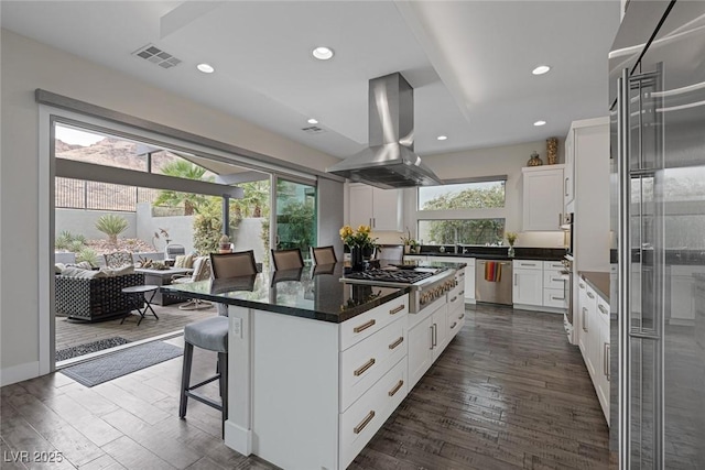 kitchen with island range hood, white cabinets, a kitchen island, a breakfast bar, and stainless steel appliances