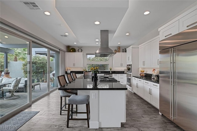 kitchen with white cabinets, a center island, island exhaust hood, stainless steel appliances, and hardwood / wood-style flooring