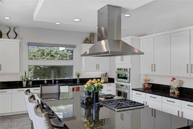 kitchen with white cabinetry, island exhaust hood, dark stone counters, sink, and light hardwood / wood-style flooring