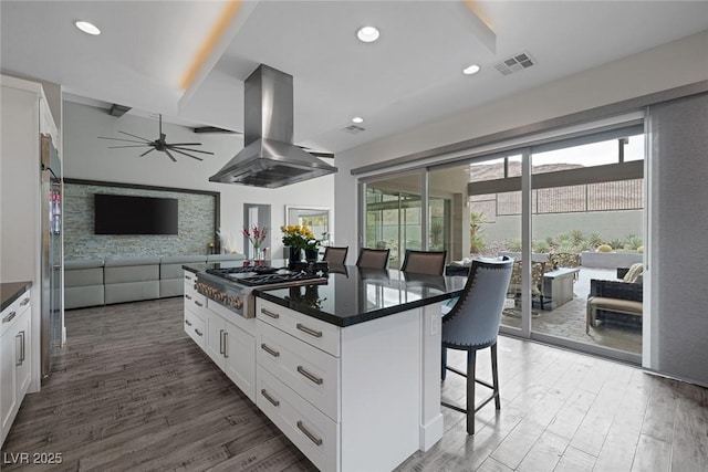 kitchen with white cabinets, a kitchen bar, stainless steel gas stovetop, and island exhaust hood