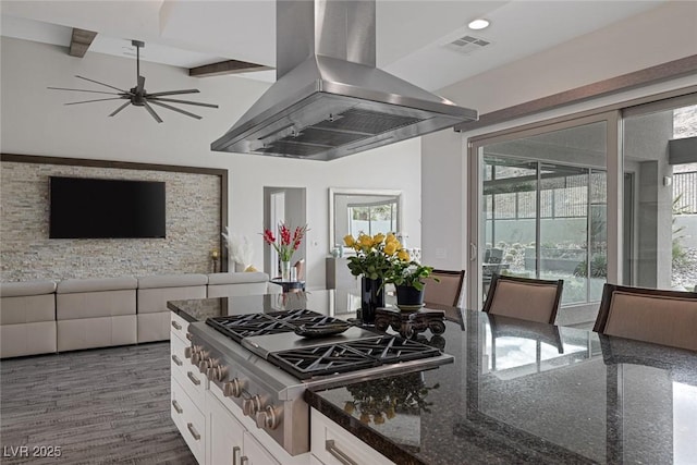 kitchen featuring white cabinetry, island exhaust hood, dark stone counters, vaulted ceiling with beams, and stainless steel gas cooktop