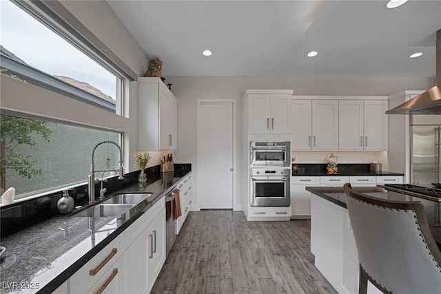 kitchen with dark stone counters, white cabinets, light wood-type flooring, sink, and stainless steel appliances