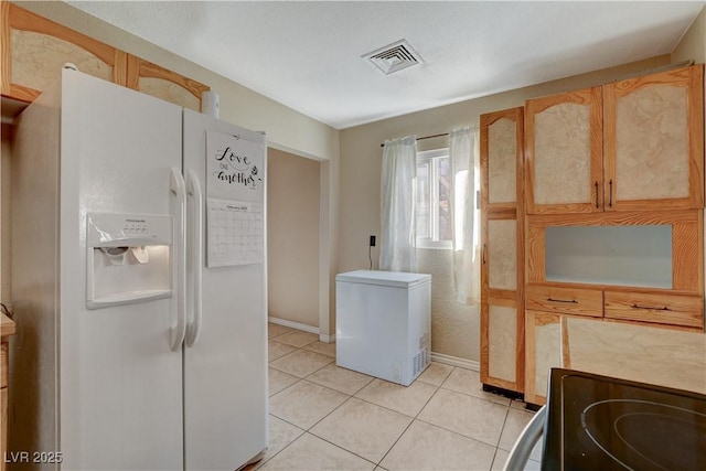 kitchen with white refrigerator with ice dispenser, light tile patterned floors, light brown cabinetry, and refrigerator