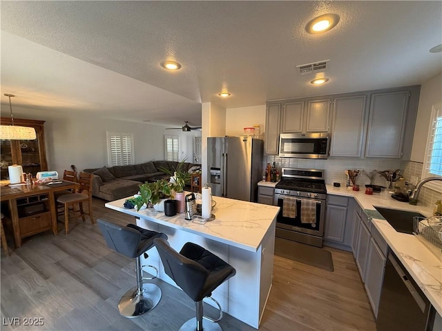 kitchen featuring appliances with stainless steel finishes, hanging light fixtures, sink, a breakfast bar area, and gray cabinets