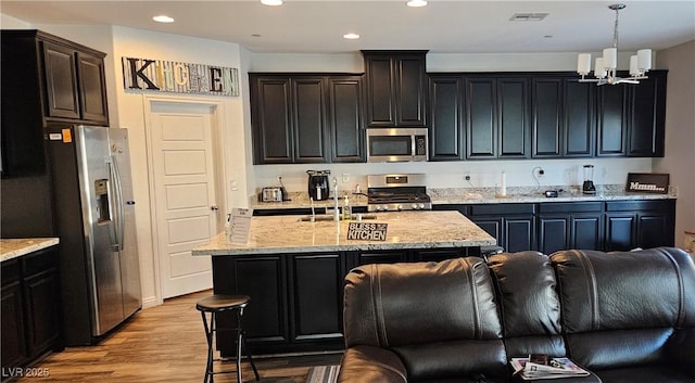 7050 Fossil Rim St, Las Vegas, NV 89084 - kitchen with stainless steel appliances, a chandelier, light stone countertops, light wood-type flooring, and an island with sink