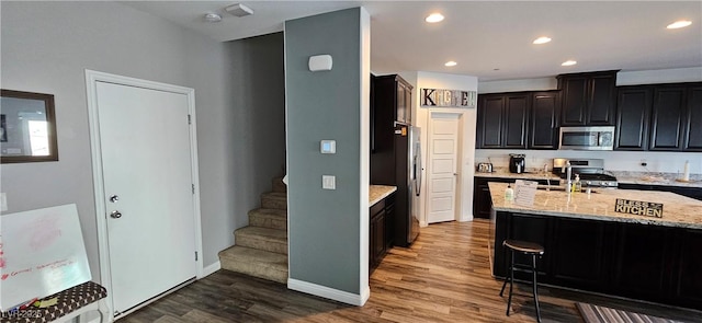 7050 Fossil Rim St, Las Vegas, NV 89084 - kitchen with appliances with stainless steel finishes, wood finished floors, light stone counters, a sink, and a kitchen bar