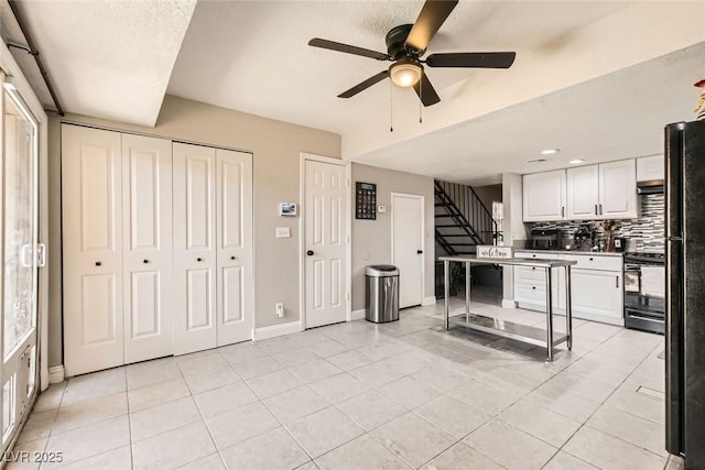 kitchen with light tile patterned floors, electric range oven, white cabinets, and tasteful backsplash