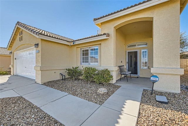 property entrance with stucco siding, concrete driveway, an attached garage, and a tiled roof