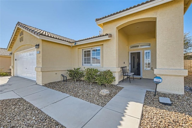 entrance to property with stucco siding, a tiled roof, and an attached garage