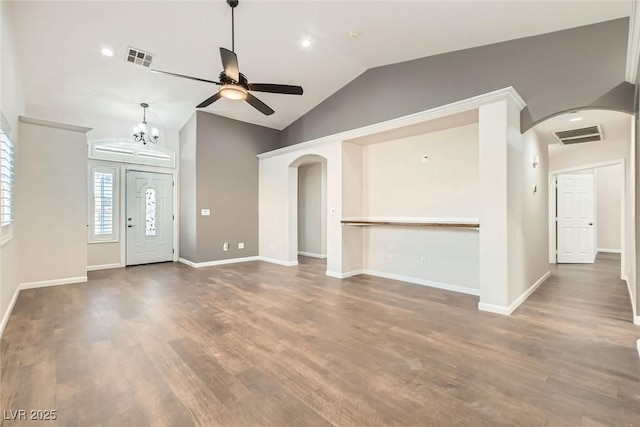 unfurnished living room with lofted ceiling, wood finished floors, visible vents, and arched walkways