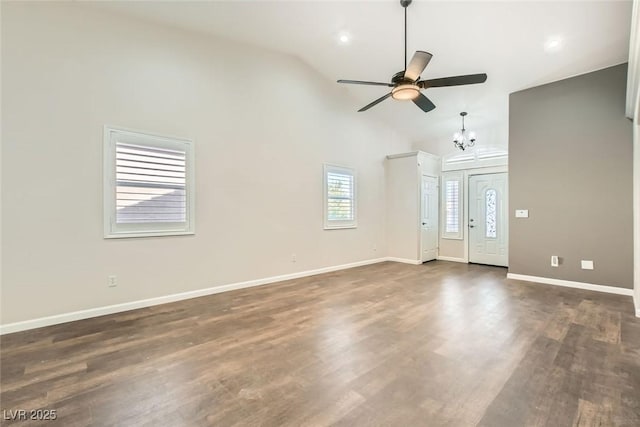 unfurnished living room with baseboards, high vaulted ceiling, dark wood-style flooring, and ceiling fan with notable chandelier