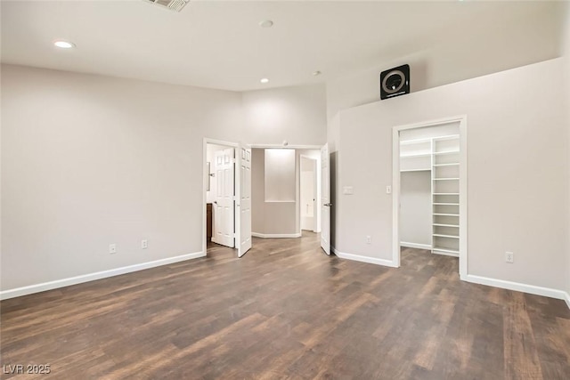 unfurnished bedroom with recessed lighting, a walk in closet, baseboards, and dark wood-type flooring