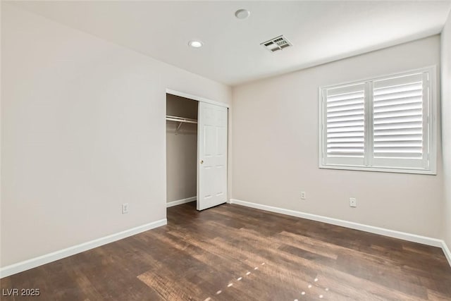 unfurnished bedroom featuring visible vents, baseboards, a closet, and dark wood-style flooring