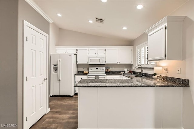 kitchen with dark stone counters, vaulted ceiling, a peninsula, white appliances, and a sink