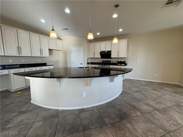 kitchen featuring sink, a breakfast bar, white cabinetry, stainless steel range, and an island with sink