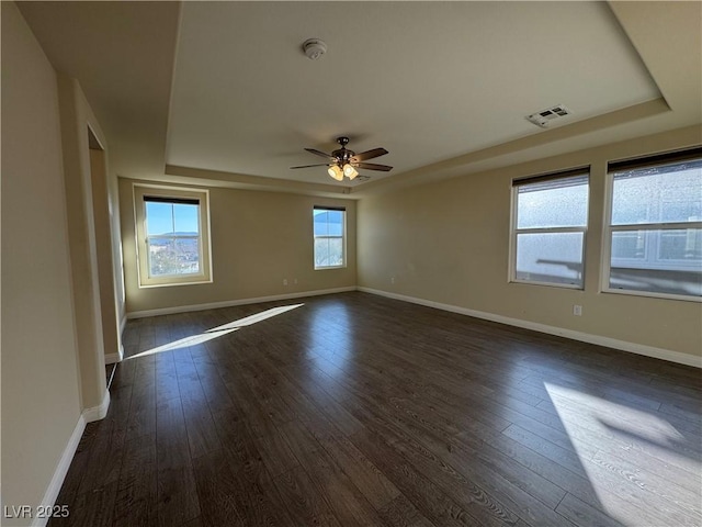 empty room featuring ceiling fan, a tray ceiling, and dark hardwood / wood-style floors